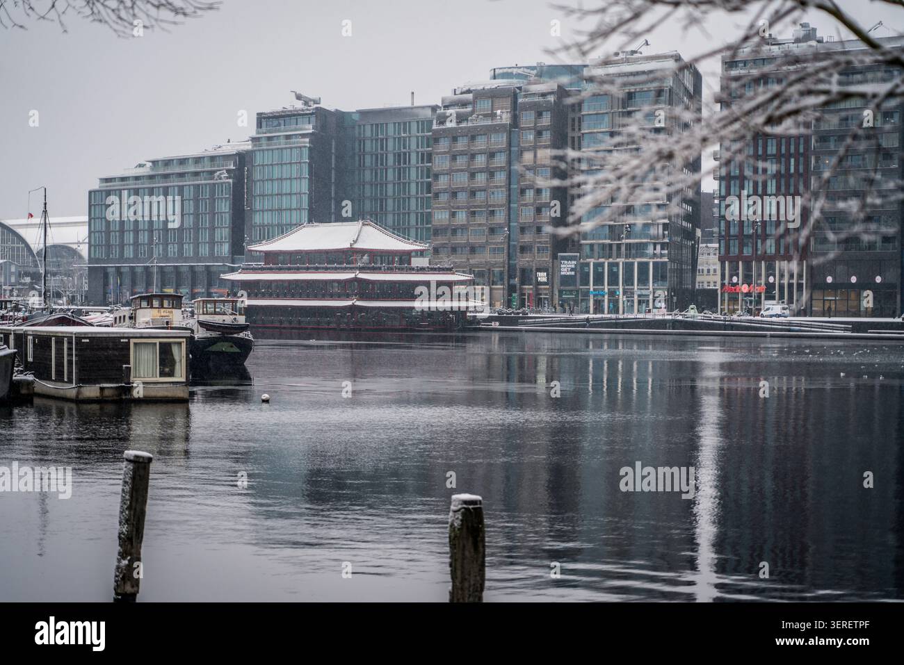 Una tranquilla scena invernale cattura il ristorante galleggiante del Sea Palace, immerso nella neve, accanto ai moderni edifici sul lungomare di Amsterdam, Paesi Bassi. Housebo Foto Stock