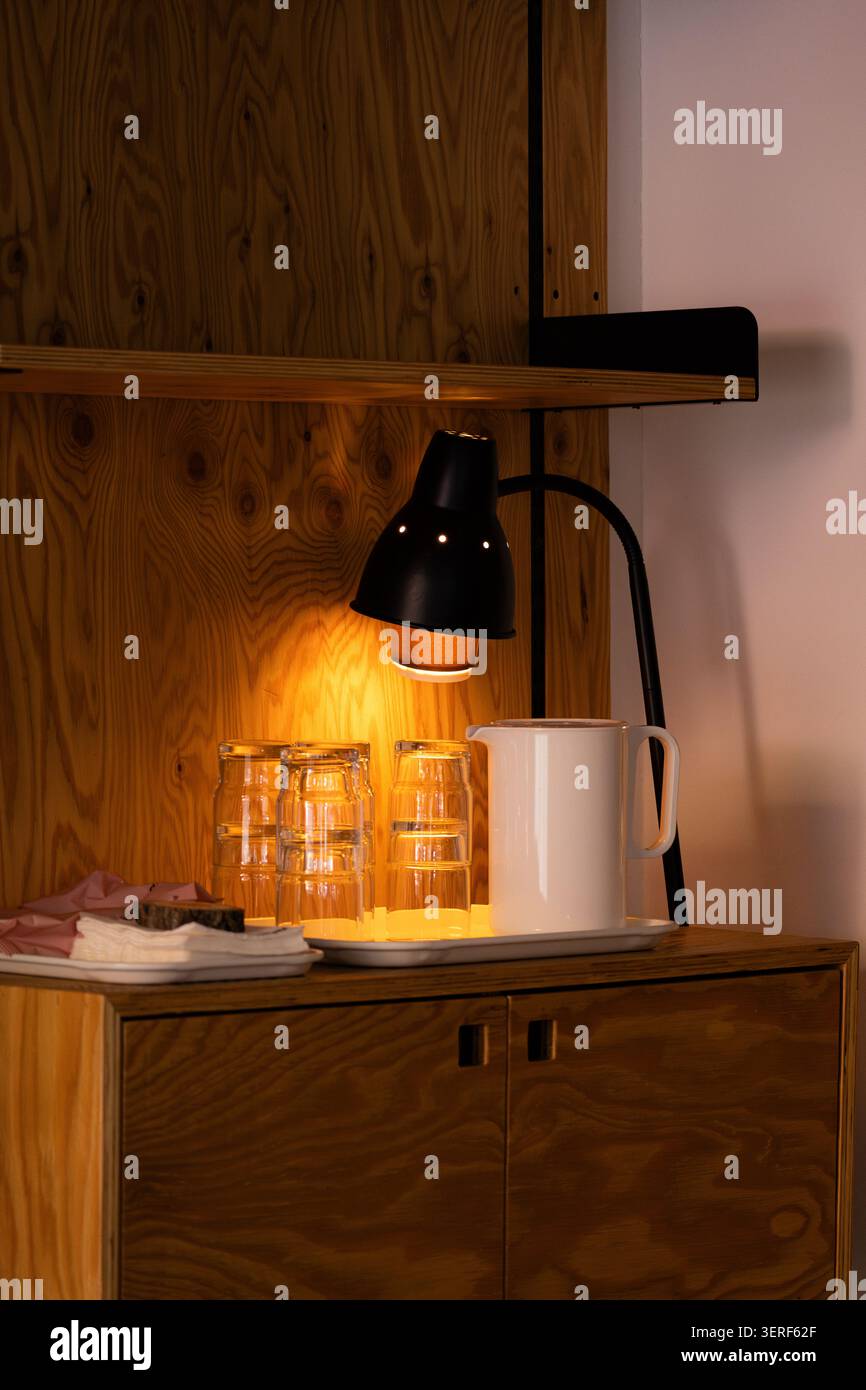 Primo piano di una calda lampada vintage che illumina una caraffa d'acqua e dei bicchieri su un armadietto di legno Foto Stock