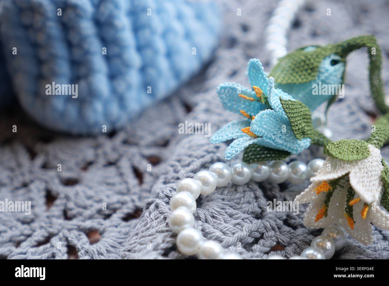 Fiori colorati e una collana di perle poggiano su un tappeto grigio all'uncinetto Foto Stock