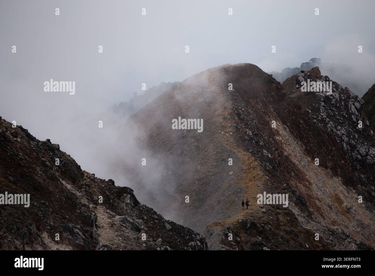 Due escursionisti sulla cresta rocciosa nebbiosa del monte Sibayak, un vulcano attivo vicino a Berastagi, Sumatra settentrionale, Indonesia, all'alba Foto Stock