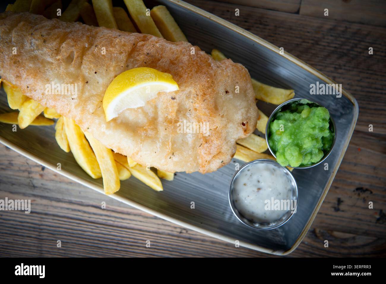 Delizioso pesce e patatine fritte servite calde su un tavolo di legno rustico Foto Stock