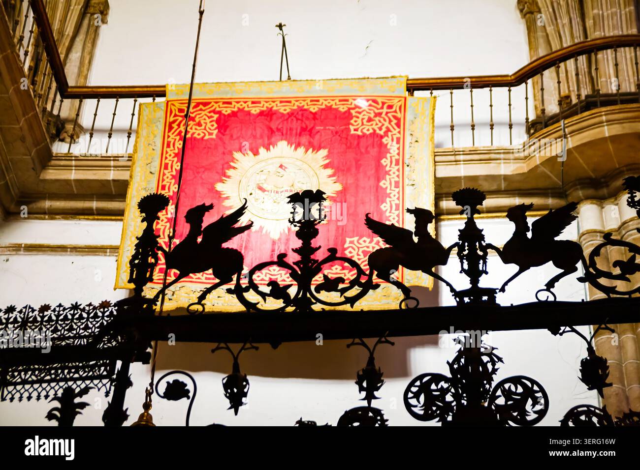 Un dettagliato primo piano di un intricato cancello in ferro battuto nero con sagome mitiche di creature alate, ambientato contro una chiesa rossa e dorata Foto Stock