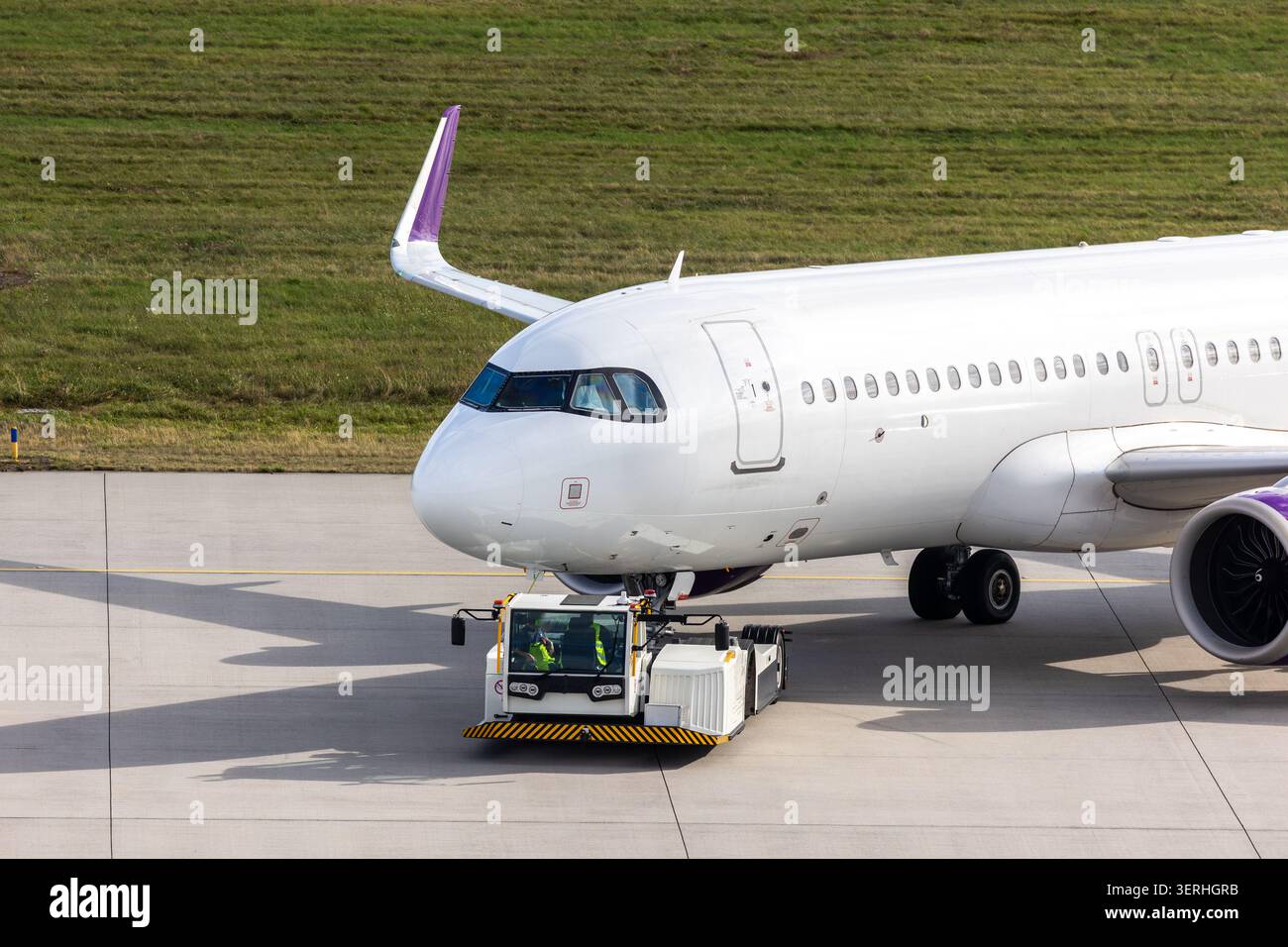 Moderno aereo regionale trainato da un veicolo a terra sulla pista di rullaggio dell'aeroporto sotto la luce del sole. Cabina di pilotaggio del motore con equipaggio chiaramente visibile che esegue operazioni tecniche Foto Stock