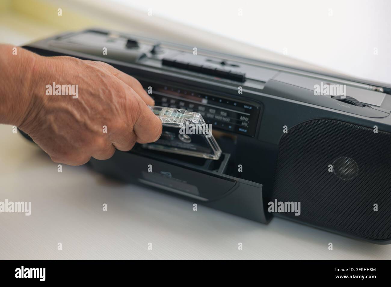 Mano collocando una cassetta audio chiara in un vecchio sistema stereo portatile, collegandolo a un'era del suono ormai passata Foto Stock