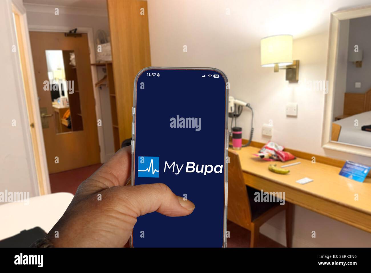 Mano che tiene in mano un telefono cellulare che mostra l'applicazione My Bupa Healthcare & Insurance in una stanza d'albergo Foto Stock