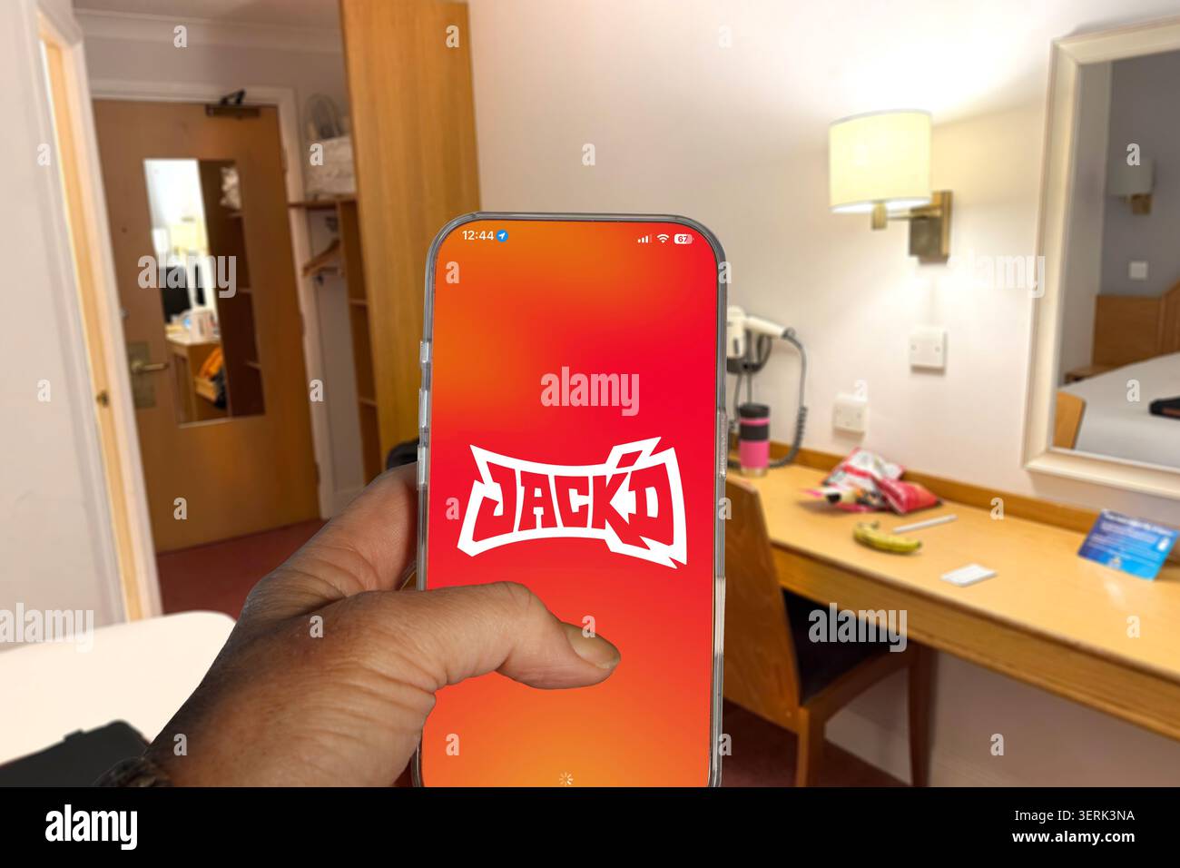 Tenere a mano l'iPhone che mostra l'app di collegamento gay il logo dell'app Jack's all'interno della camera d'albergo Foto Stock