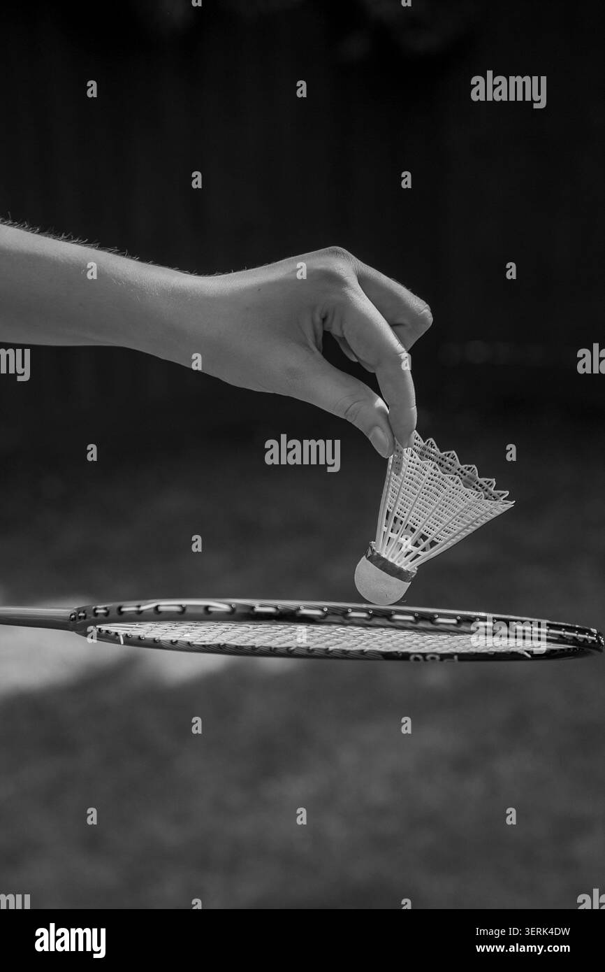 Persona che tiene un rubinetto bianco sopra una racchetta di badminton su un prato verde, apparendo pronta per servire e iniziare una partita. Foto Stock