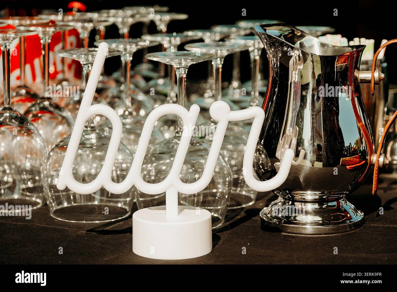 Un cartello da bar accanto a bicchieri da bibita e una caraffa durante un evento all'aperto durante il giorno. cartello da bar sul tavolo accanto alla pila di bicchieri da bibita trasparenti e metallo pi Foto Stock