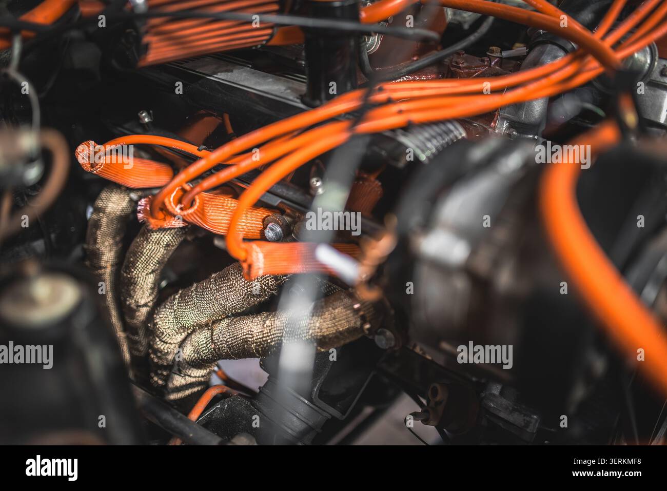 Immagine dettagliata di fili di accensione arancione vibranti e involucro di scarico resistente al calore sui componenti del motore a combustione interna di un veicolo Foto Stock