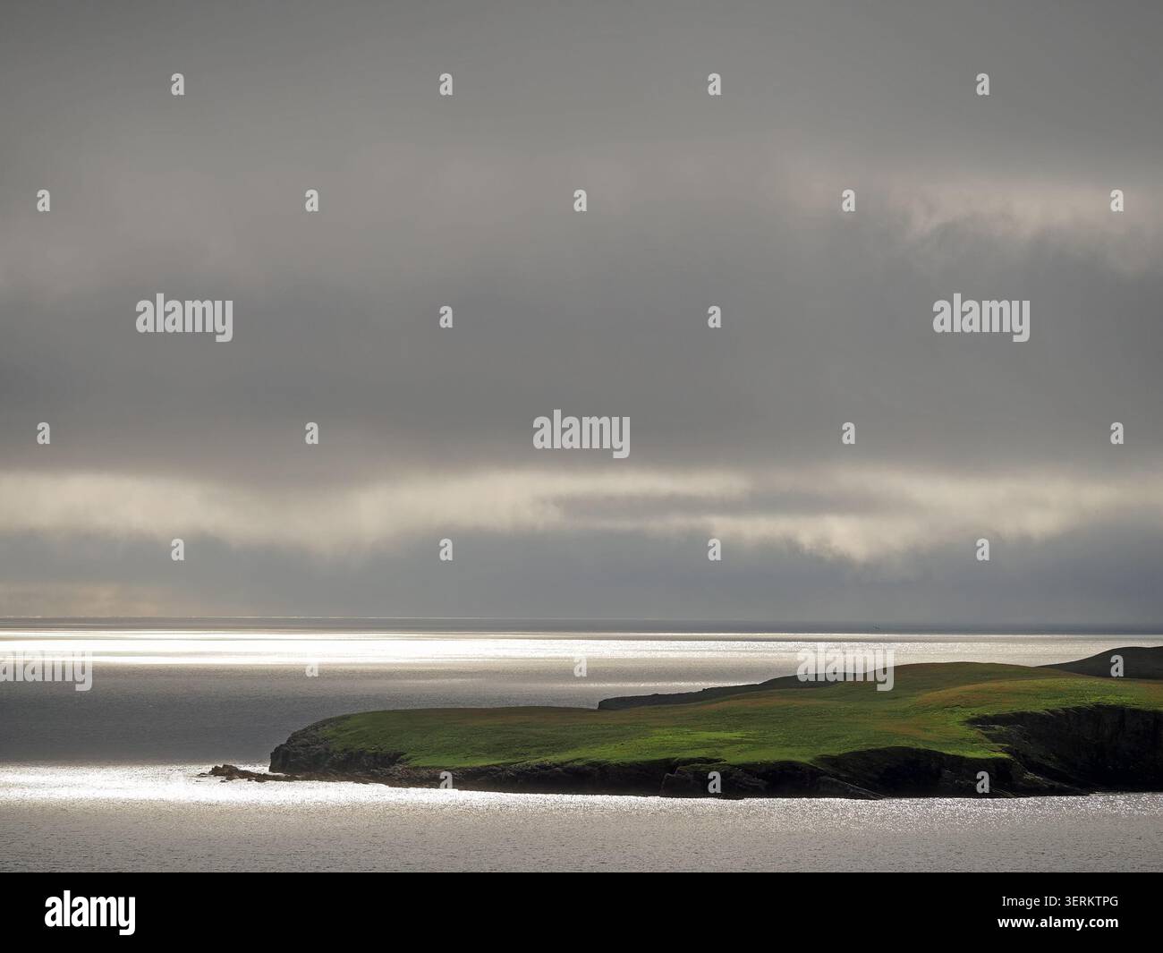 Vista mare con luce d'argento sul mare e promontorio ondulato verde di Mousa sotto un cielo grigio mooso al largo della costa orientale delle Shetland, Scozia, Regno Unito Foto Stock