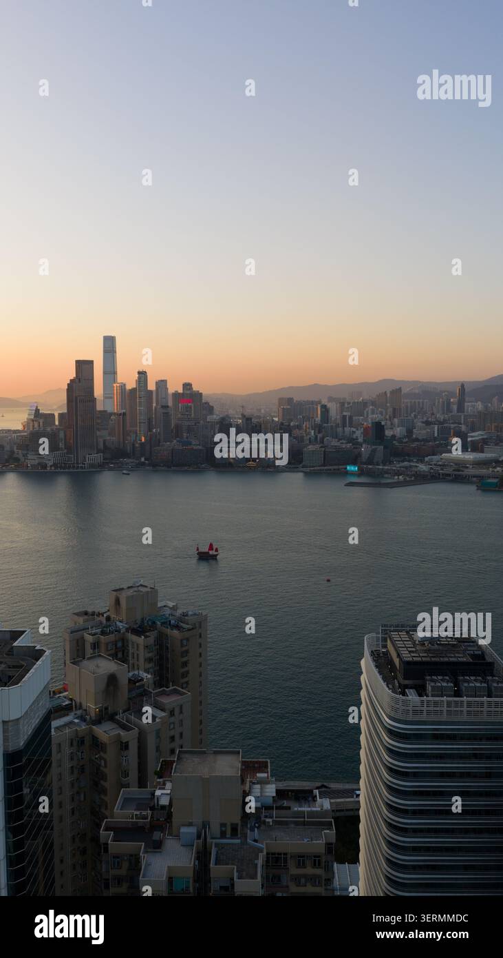Hong Kong - 14 febbraio 2026: Vista aerea dello skyline del Victoria Harbour con grattacieli e una tradizionale junk boat a vela rossa al tramonto a ho Foto Stock