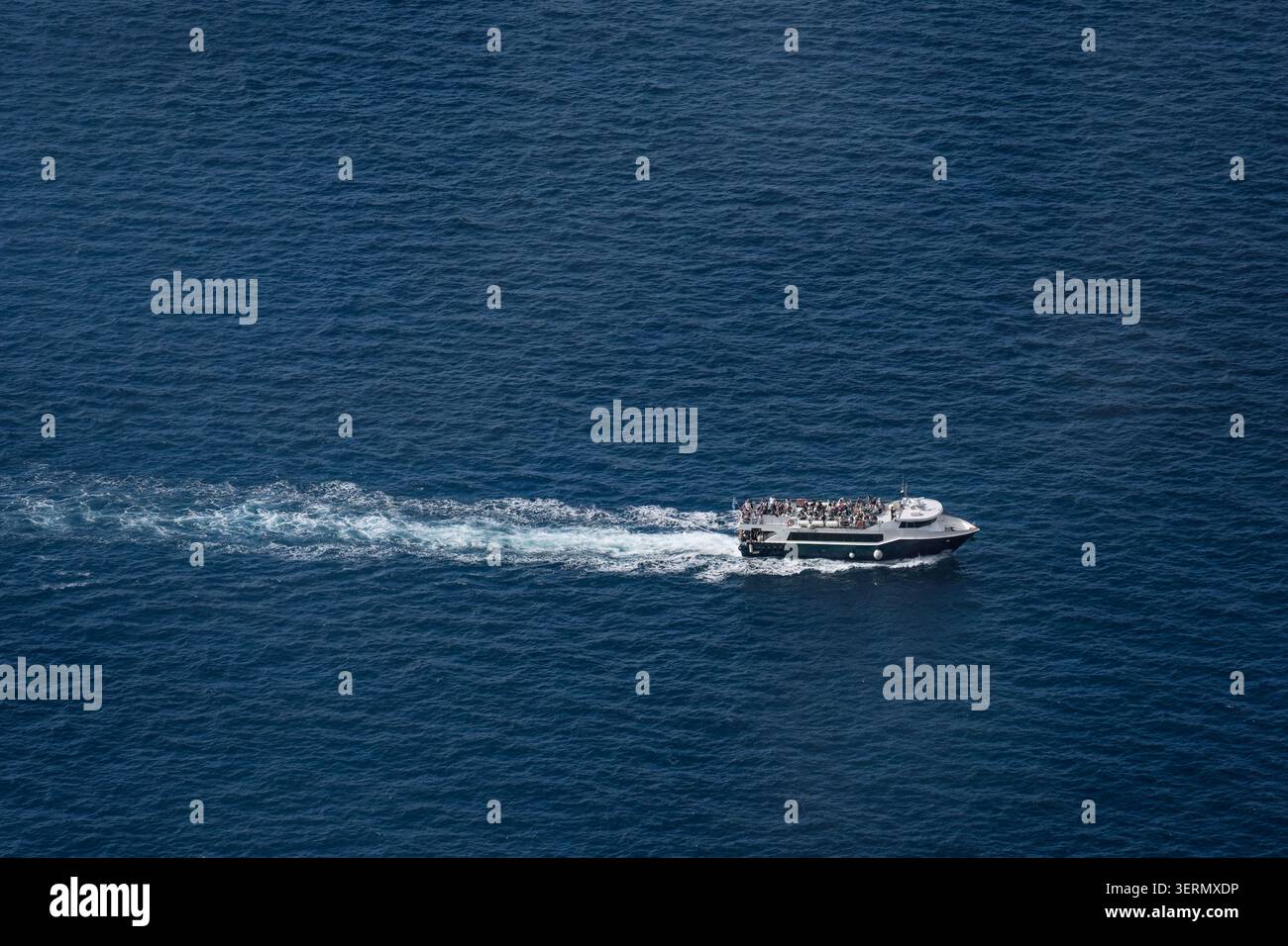 Un'imbarcazione piena di turisti lascia dietro di sé una scia bianca mentre viaggia su un mare blu. Foto Stock