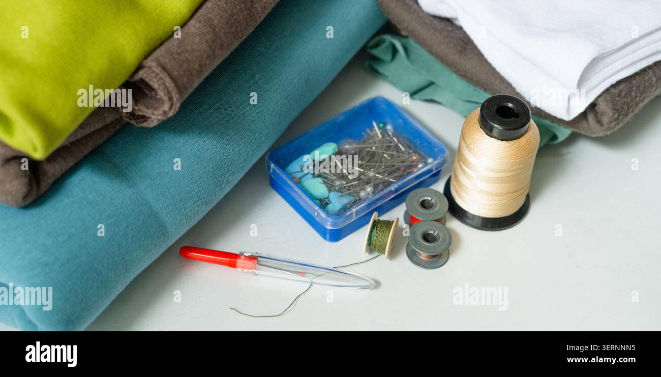 Tessuti e fili disposti su un'area di lavoro bianca come kit di cucito completo. Articoli da cucire per iniziare a divertirsi con gli hobby. Ispira una collezione di articoli essenziali per la lavorazione del tessuto per progetti fai da te Foto Stock