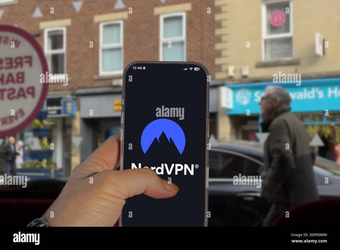 Mano che tiene in mano uno smartphone che visualizza il logo NordVPN sullo schermo con sullo sfondo una strada del Regno Unito sfocata Foto Stock