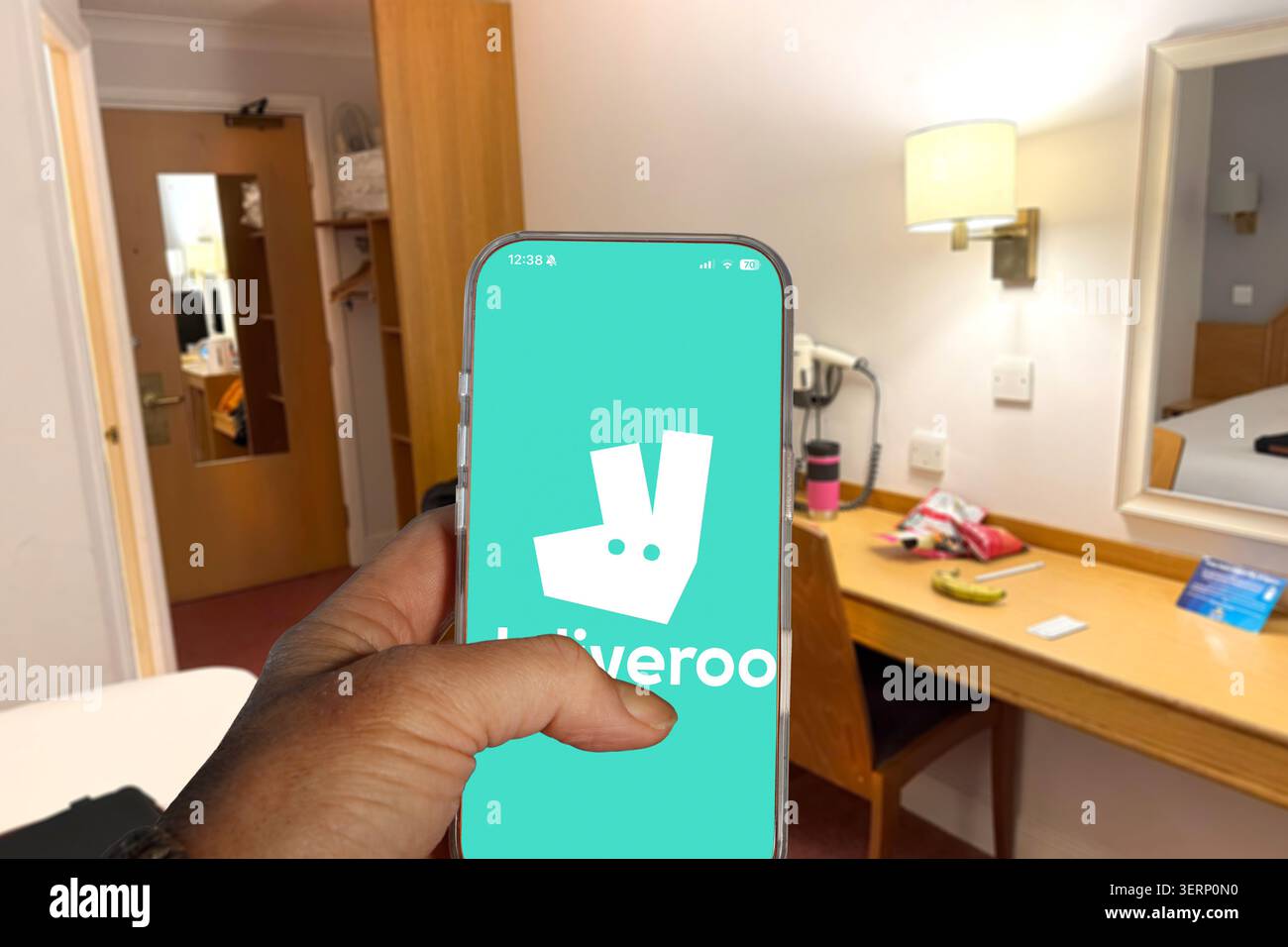 Mano con uno smartphone che mostra il logo dell'app Deliveroo in una camera d'albergo Foto Stock
