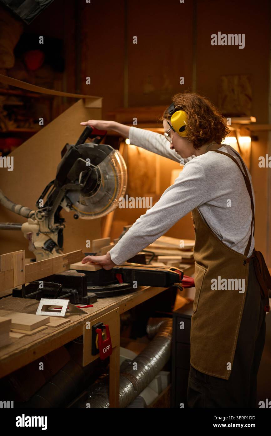 Donna adulta che utilizza la sega circolare nel laboratorio di falegnameria Foto Stock