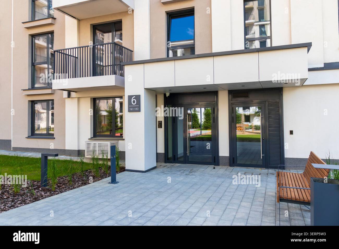 Cortile pavimentato con panca minimalista e cestino fuori da un nuovo blocco residenziale Foto Stock