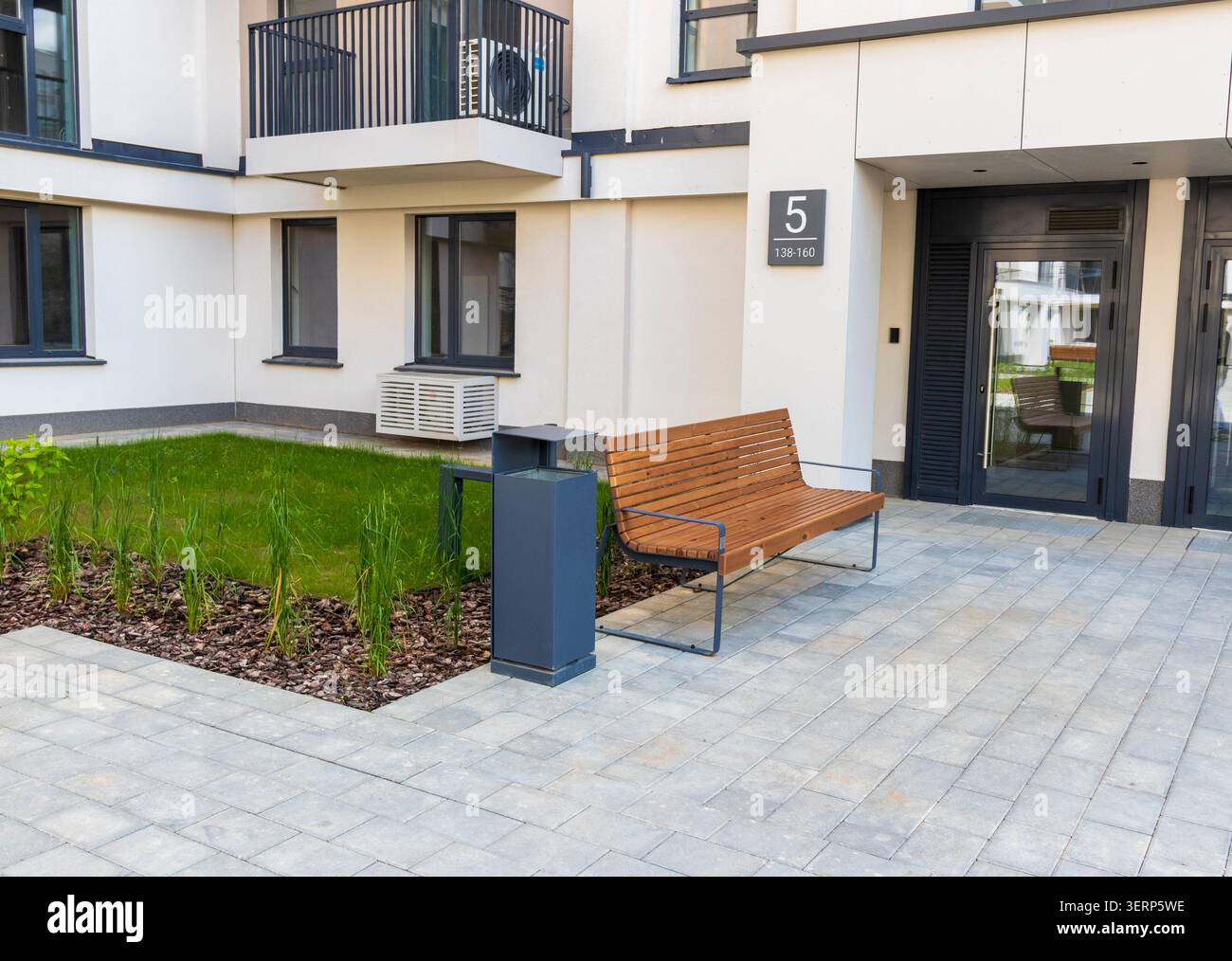 Cortile pavimentato con panca minimalista e cestino fuori da un nuovo blocco residenziale Foto Stock