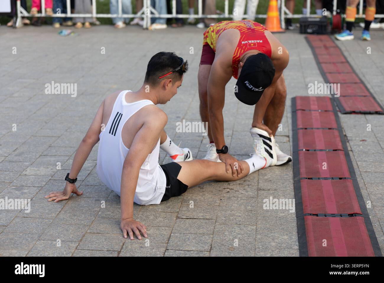 Da Lat, Vietnam - 6 giugno 2026: Un partecipante aiuta un altro corridore a prolungarsi dopo aver completato il Dalat Music Night Run 2026 a da Lat, Vietnam Foto Stock