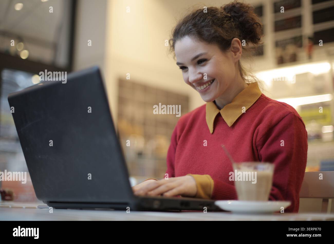 Giovane donna felice che lavora al computer portatile al bar Foto Stock