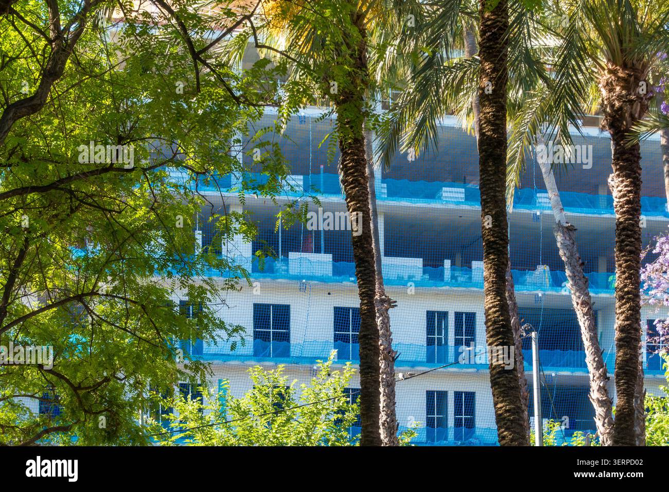 Edificio residenziale in costruzione con rete protettiva blu e alberi Foto Stock