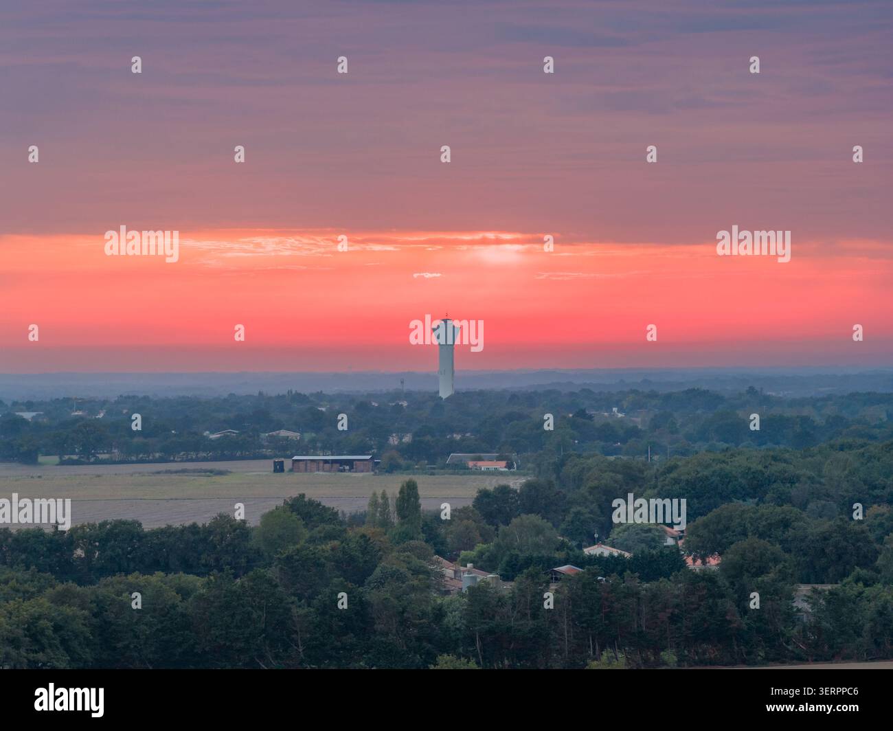 Sagomato contro un cielo rosa e arancione su campi, alberi e case sparse, Mache, Francia Foto Stock