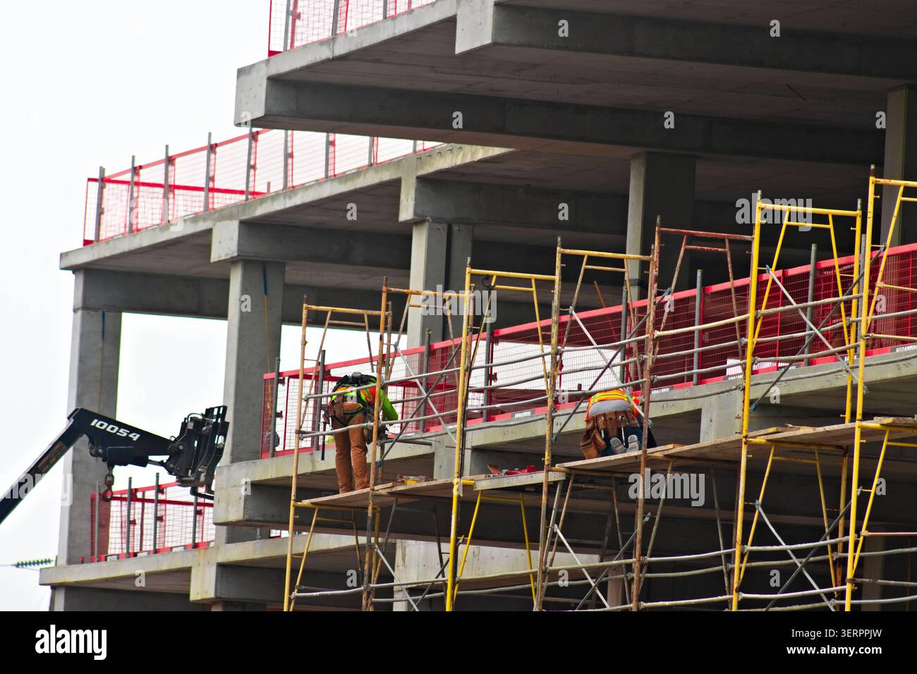 I lavoratori edili installano ponteggi lungo il bordo di una struttura di cemento a più piani in un cantiere attivo a San Bernardino, in California Foto Stock