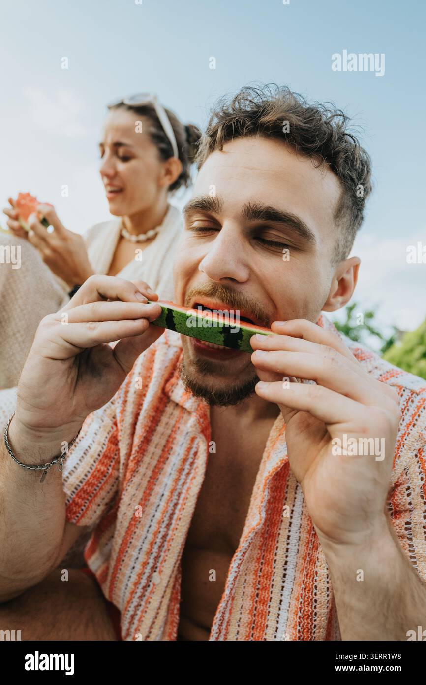 Giovane che mangia una fetta di anguria all'aperto con un amico in una giornata estiva rilassata Foto Stock