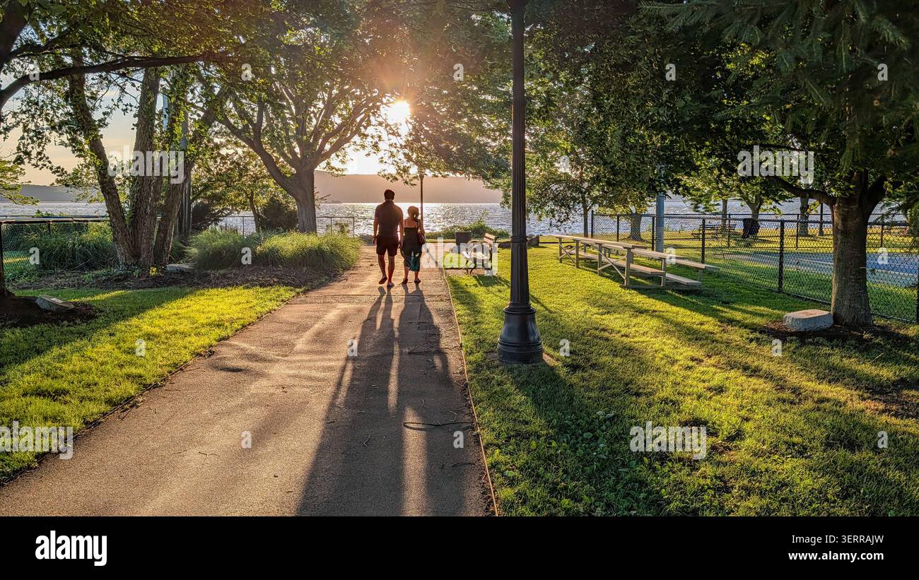 Una coppia che si gode il tramonto in un parco di Irvington, New York, getta lunghe ombre mentre passeggiano verso il fiume Hudson Foto Stock