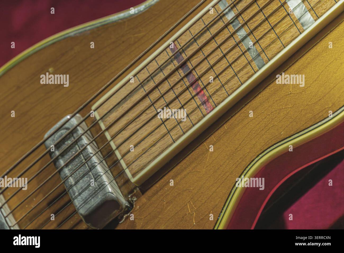 Collo e lavagna per chitarra acustica, con motivi a grana di legno chiaro, marcatori intarsiati, finitura liscia, frets usurati, sfondo in tessuto rosso, evidenziazione Foto Stock