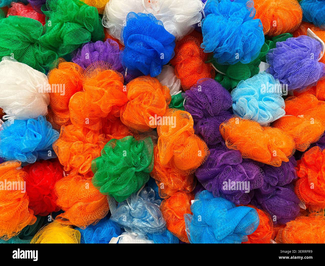Colorato assortimento di pouf in spugna da bagno in rete multicolore impilati in un mercato Foto Stock