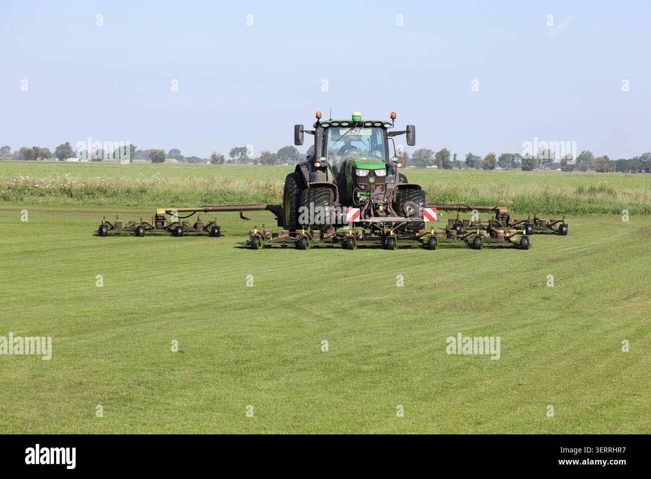 Un trattore John Deere 6155R e un rasaerba Eco Clipper tagliano l'erba sul campo di un coltivatore di erba Foto Stock