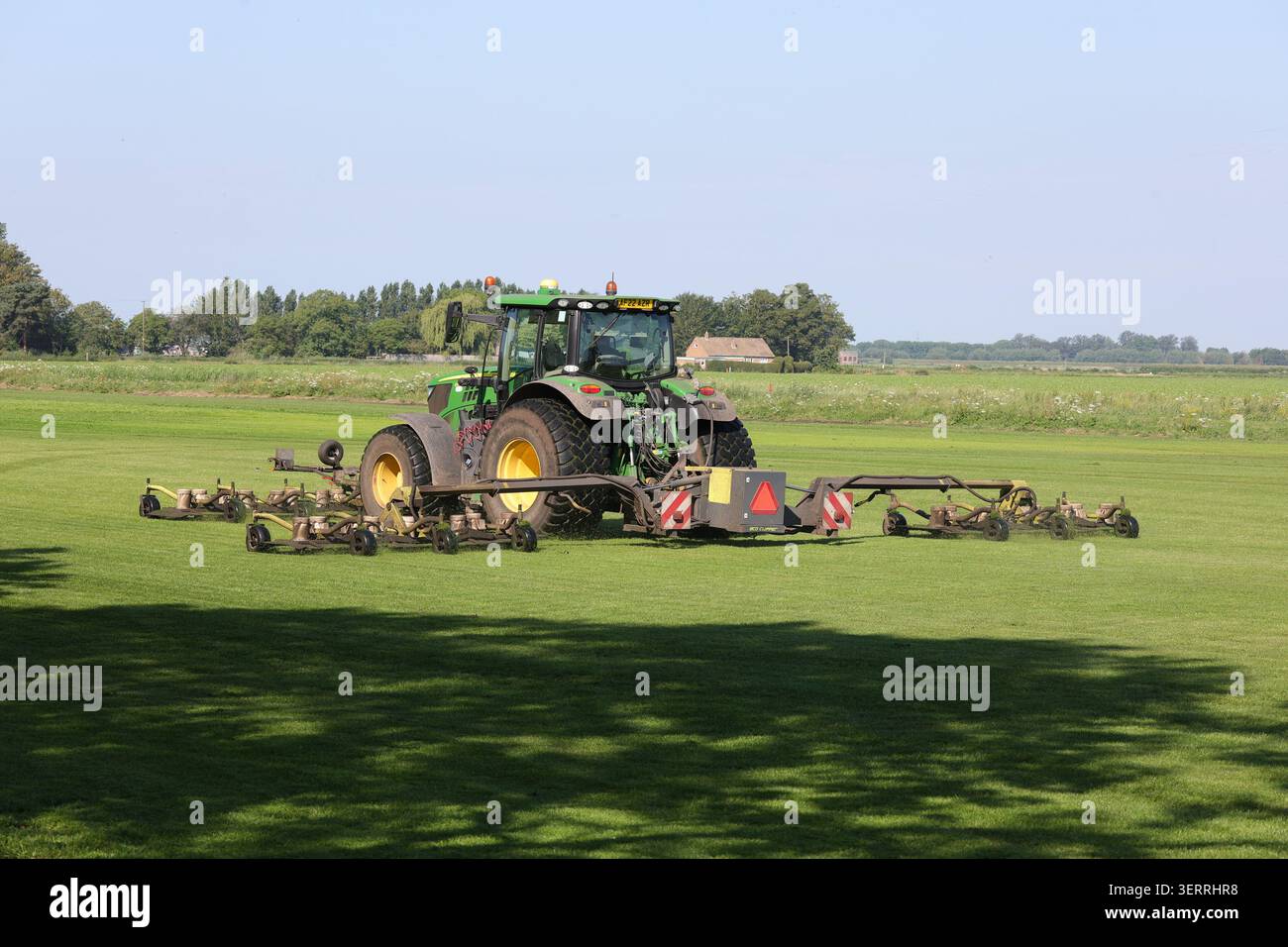 Un trattore John Deere 6155R e un rasaerba Eco Clipper tagliano l'erba sul campo di un coltivatore di erba Foto Stock
