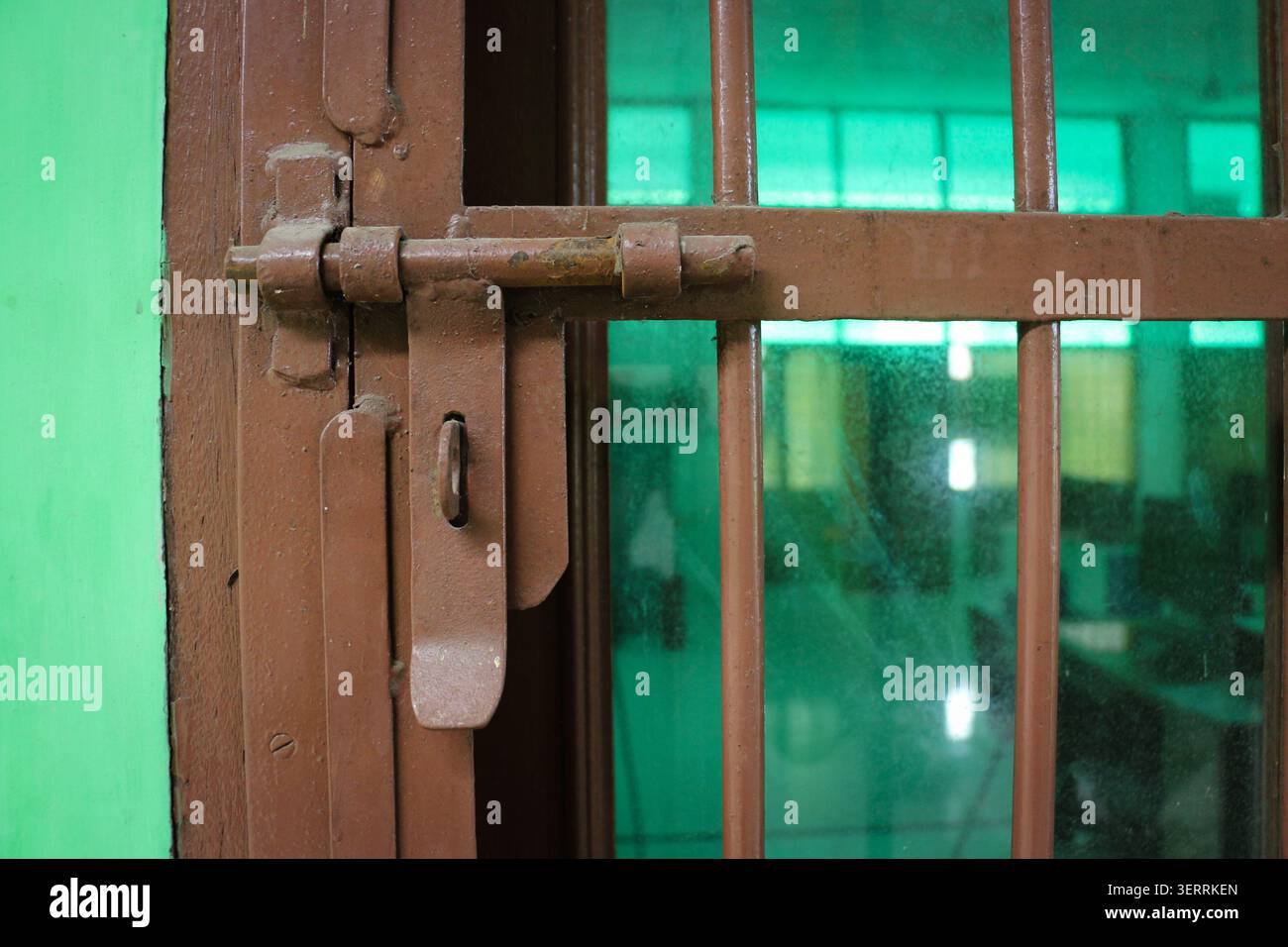 Primo piano della serratura a bullone in metallo arrugginito sulla griglia di sicurezza con finestrino in vetro, dettaglio di protezione ingresso casa, serratura in acciaio verniciato marrone e parrucchiere di sicurezza Foto Stock