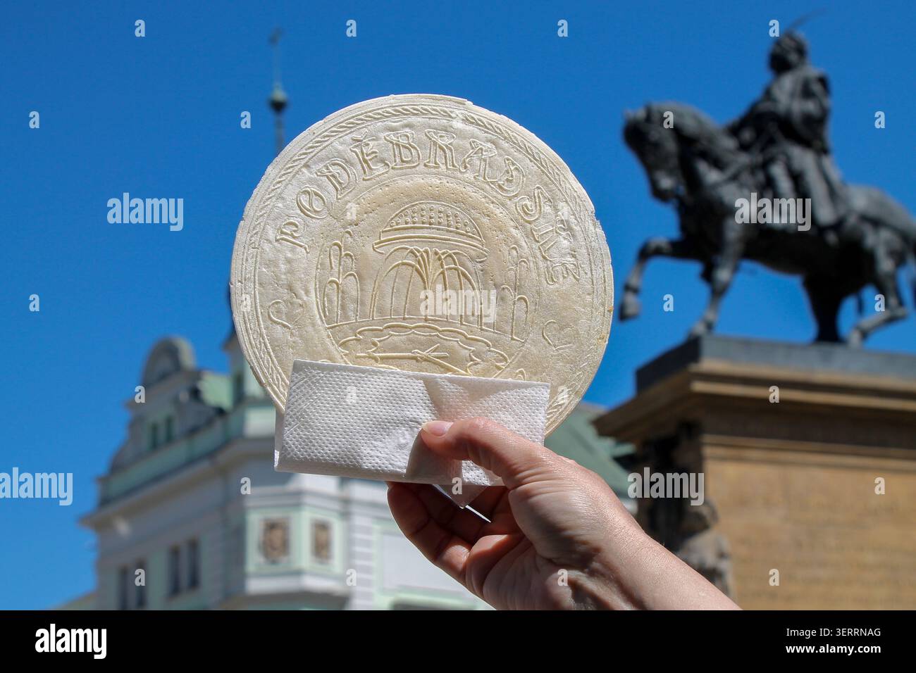 Un tipico dessert termale - un wafer rotondo tenuto in mano sullo sfondo del cielo e della piazza della città. Repubblica Ceca, Podebrady. Foto Stock