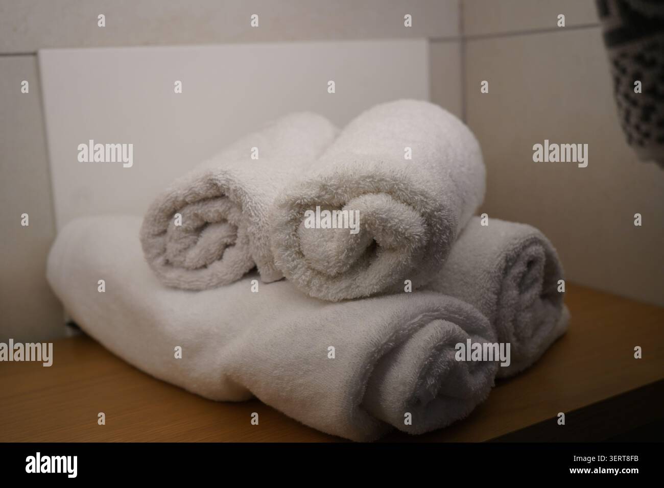Una pila di asciugamani di cotone bianco, puliti e arrotolati, collocati ordinatamente su un ripiano di legno in un bagno moderno. Servizi freschi. Foto Stock