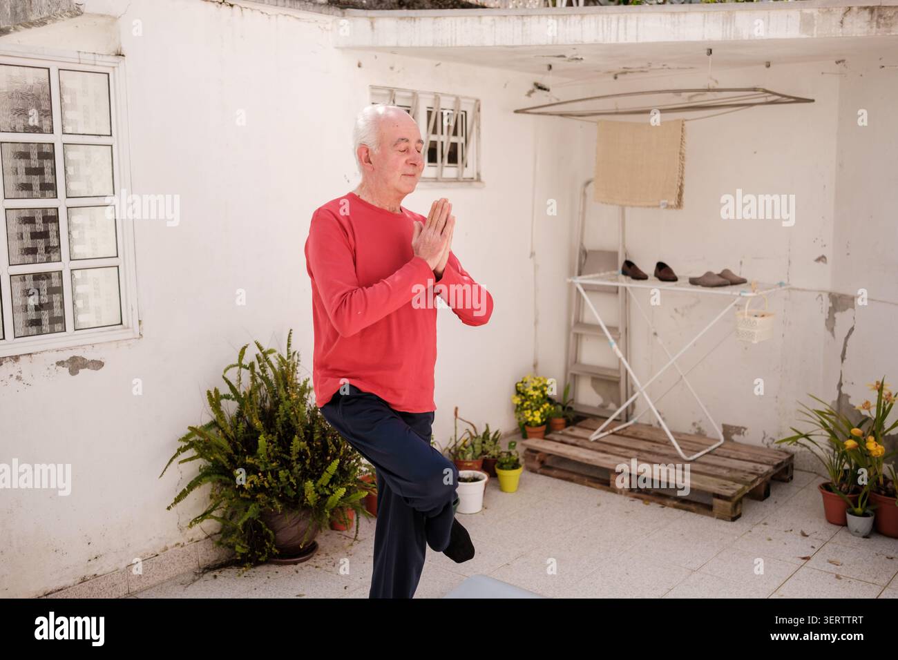 Uomo anziano in equilibrio in posa albero, abbracciando invecchiamento sano e benessere su un patio Foto Stock