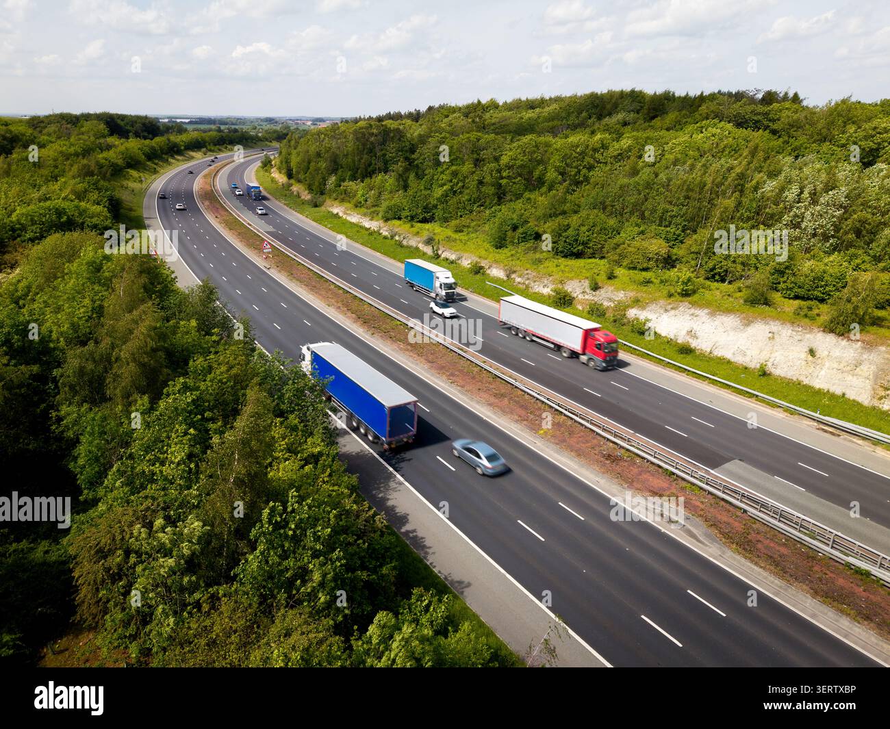 Vista aerea di un'autostrada del Regno Unito affollata, con camion e auto che attraversano un bosco di campagna che collega le principali città su un luminoso su Foto Stock