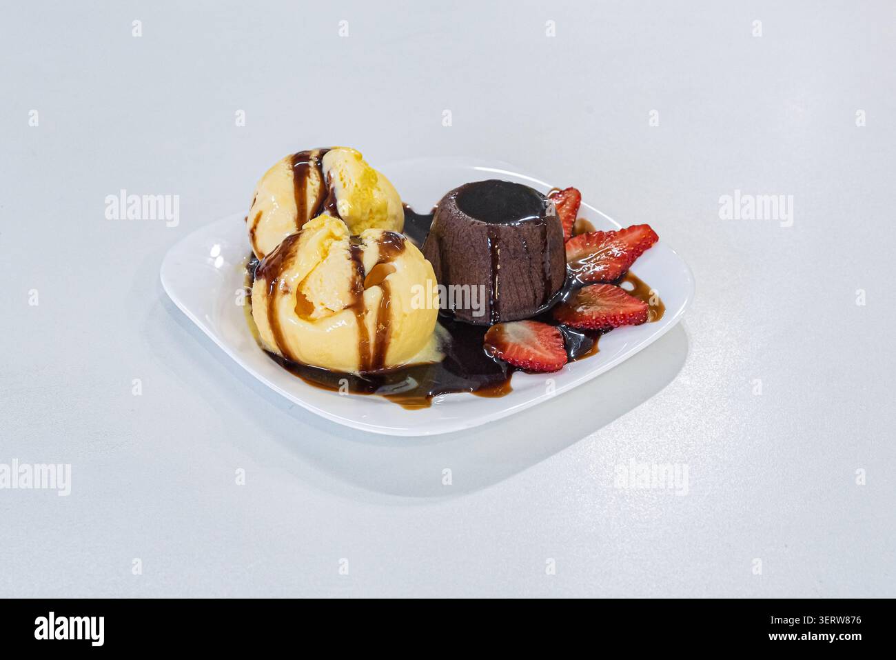 Studio shot con torta lavica servita con palline da gelato alla vaniglia e fragole fresche su piatto bianco. Dessert condito con sciroppo al cioccolato. SWE Foto Stock