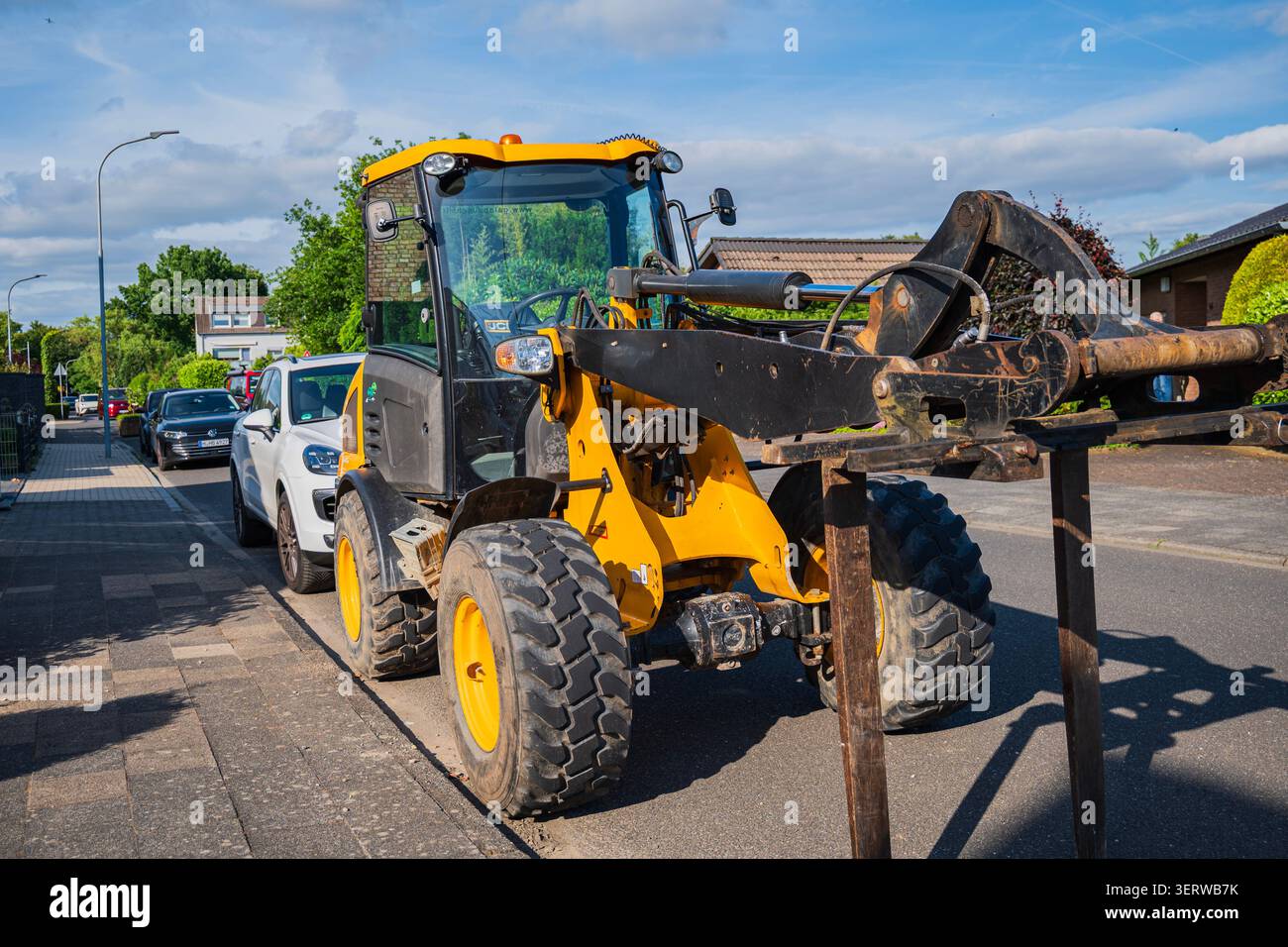 Kaarst, Germania, 10.06.2026 - pala gommata gialla piccola con attacco forche per pallet parcheggiata su una strada residenziale suburbana durante i lavori di costruzione o ro Foto Stock