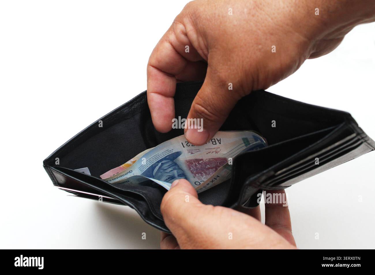 Primo piano di un paio di mani di un uomo che aprono un portafoglio nero pieno di banconote del peso messicano su uno sfondo bianco infinito. Chihuahua, Messico. Concetto: Peso Foto Stock