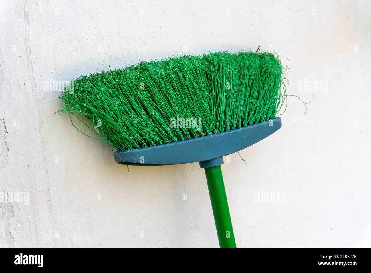 Una scopa verde è appoggiata a un muro. Foto Stock