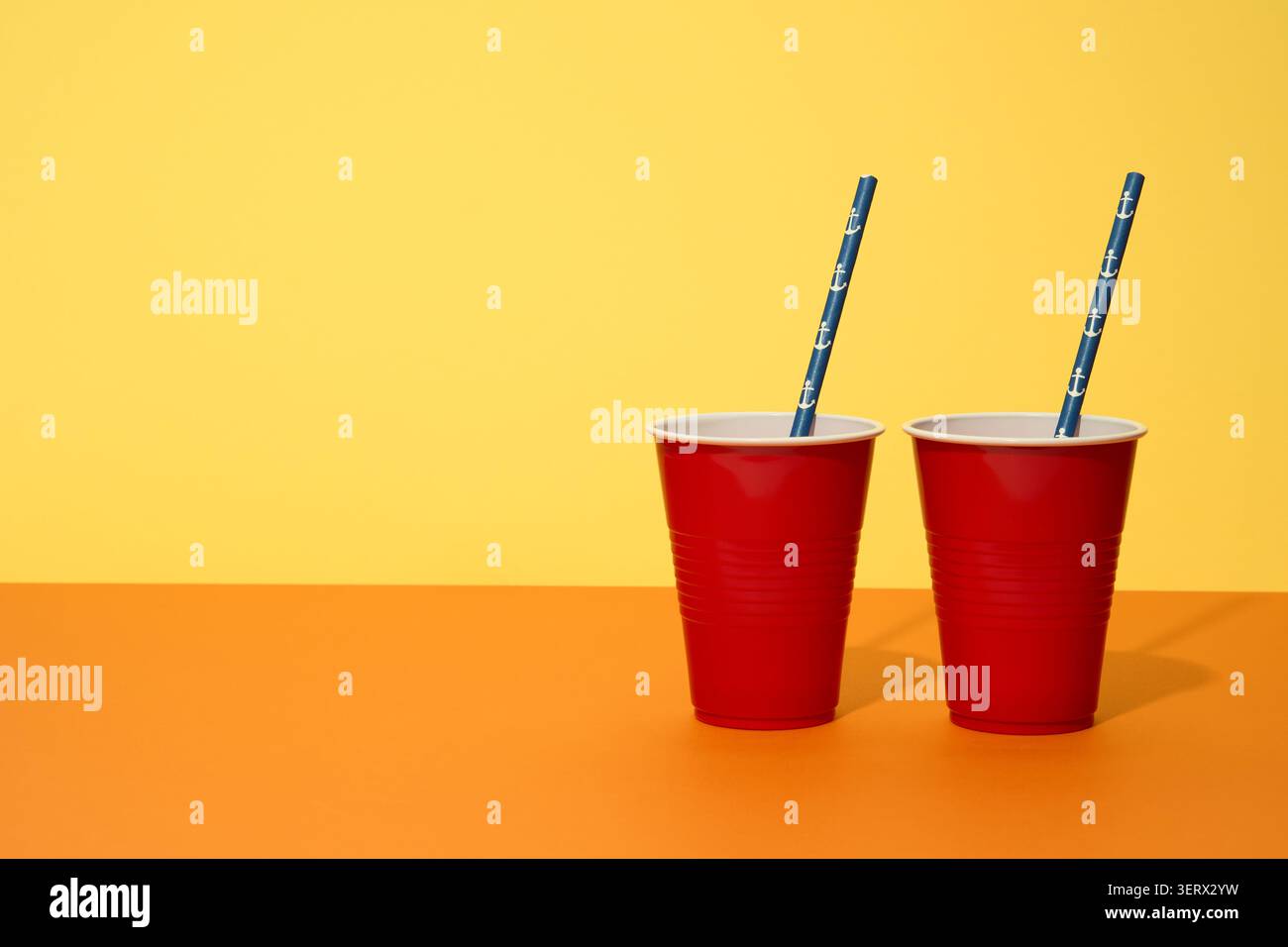 Occhiali di plastica rossi con cannucce blu su sfondo giallo. Foto Stock