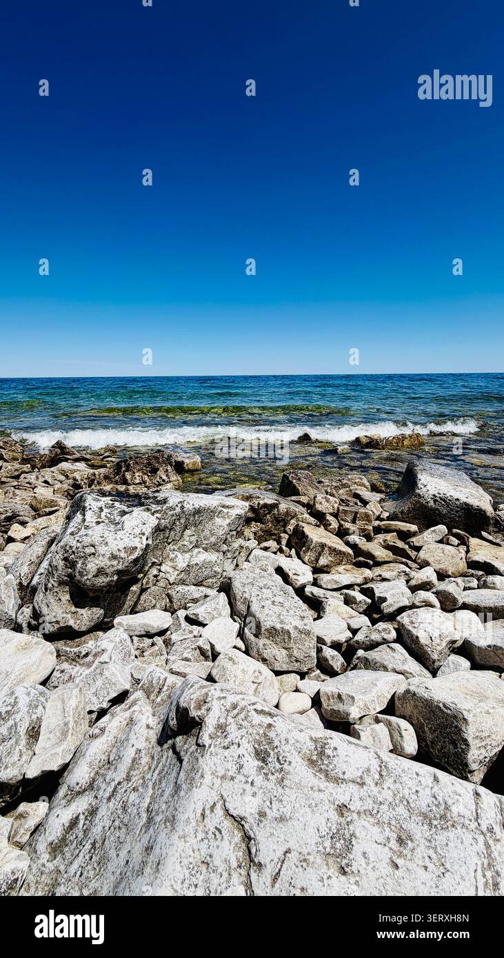 Vista panoramica di una spiaggia rocciosa con dolci onde sulla Penisola di Bruce, Canada, sotto un cielo azzurro senza nuvole, perfetto paesaggio estivo. Foto Stock