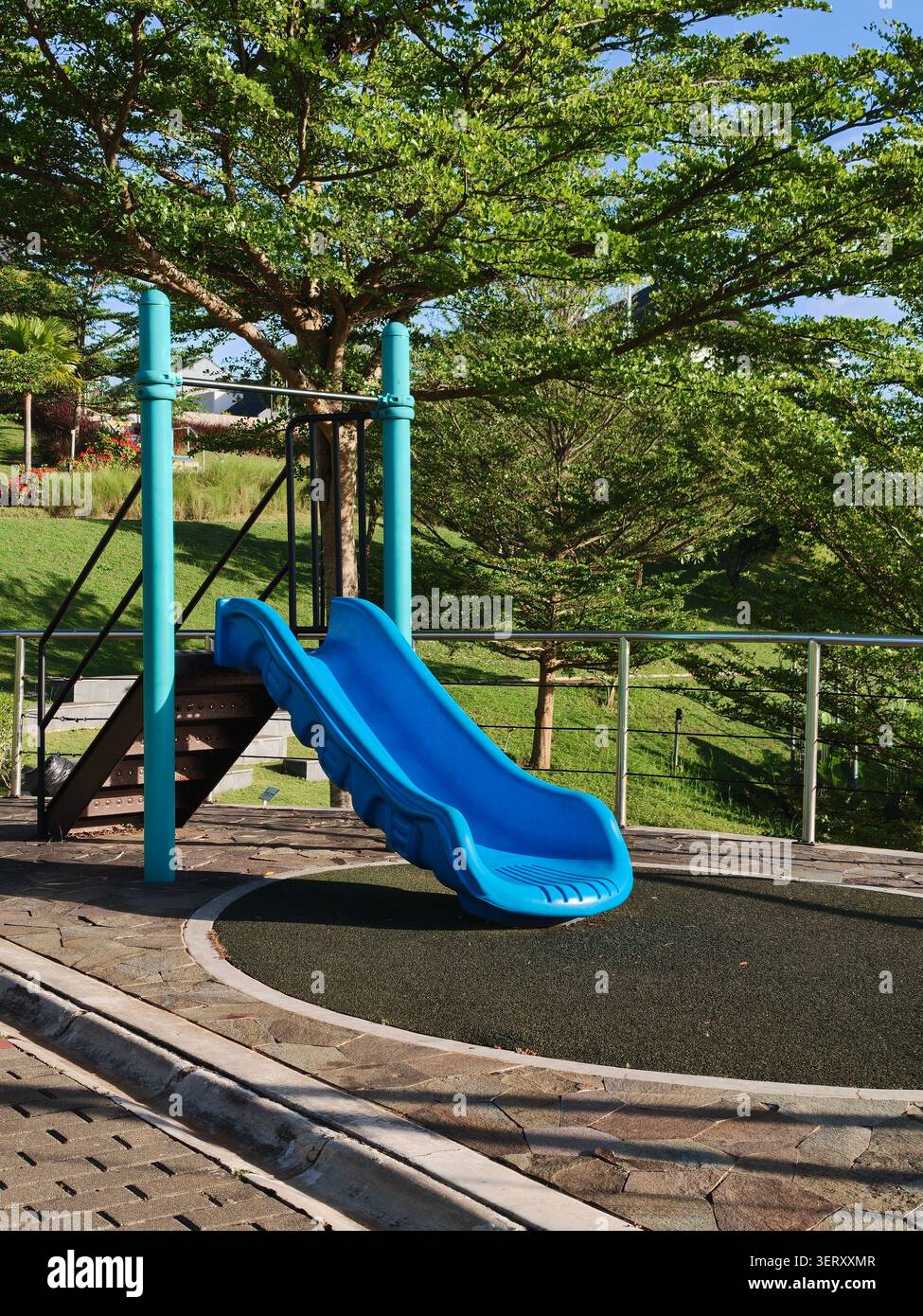Scivolo per bambini in plastica blu in un parco giochi all'aperto circondato da alberi verdi rigogliosi in una giornata soleggiata - Immagine stock catturata con smartphone
