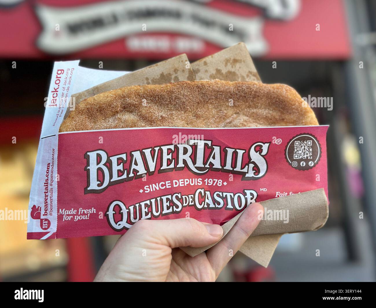 Jasper, Canada - 26 maggio 2026: Una mano tiene un dolce di pasta fritta BeaverTails, condito con cannella e zucchero. - Immagine stock catturata con smartphone