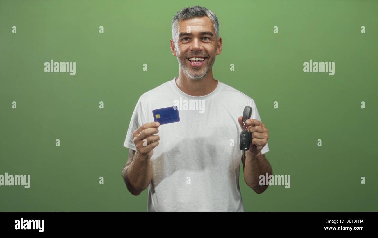 Uomo di mezza età con i capelli grigi tiene una carta di credito e le chiavi dell'auto in una mano, l'altra mano vicino al petto, gli occhi chiusi, indossa una t shirt bianca in studio; fi Foto Stock