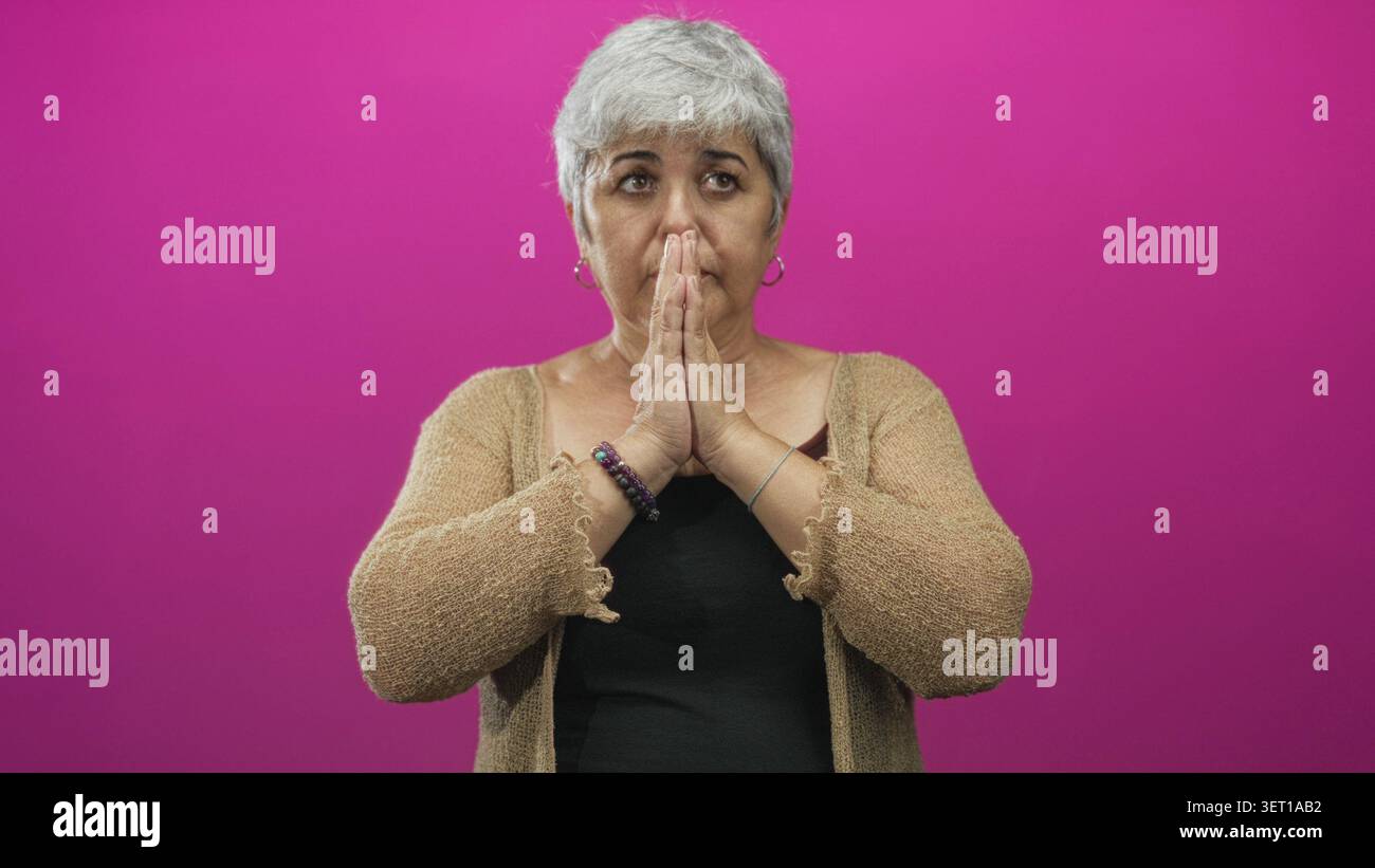 Donna anziana con le palme premuta insieme in gesto di preghiera e occhi chiusi in studio; calma riflessione. Foto Stock