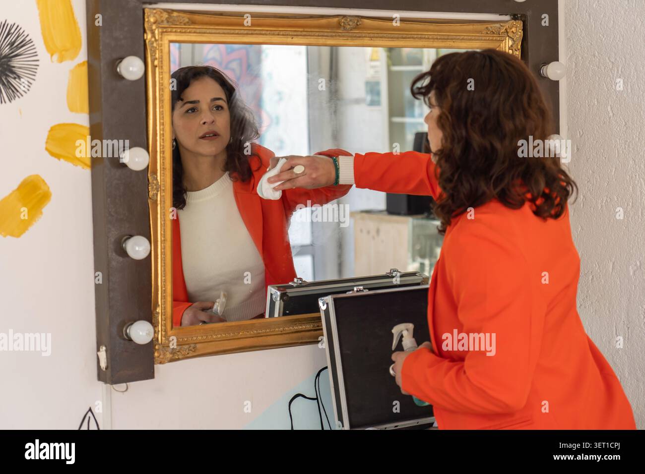 Donna che pulisce uno specchio da trucco in un salone di bellezza mentre prepara il suo spazio di lavoro prima di una sessione con il cliente. Foto Stock