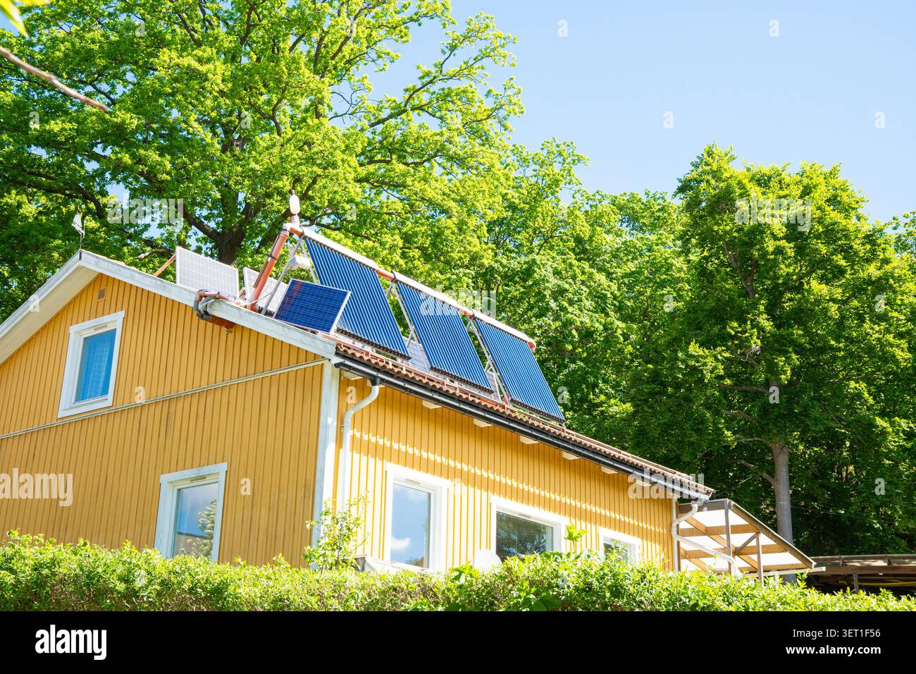Casa gialla con collettori solari termici e pannelli solari sul tetto per un'energia sostenibile e riscaldamento in una soleggiata giornata estiva Foto Stock